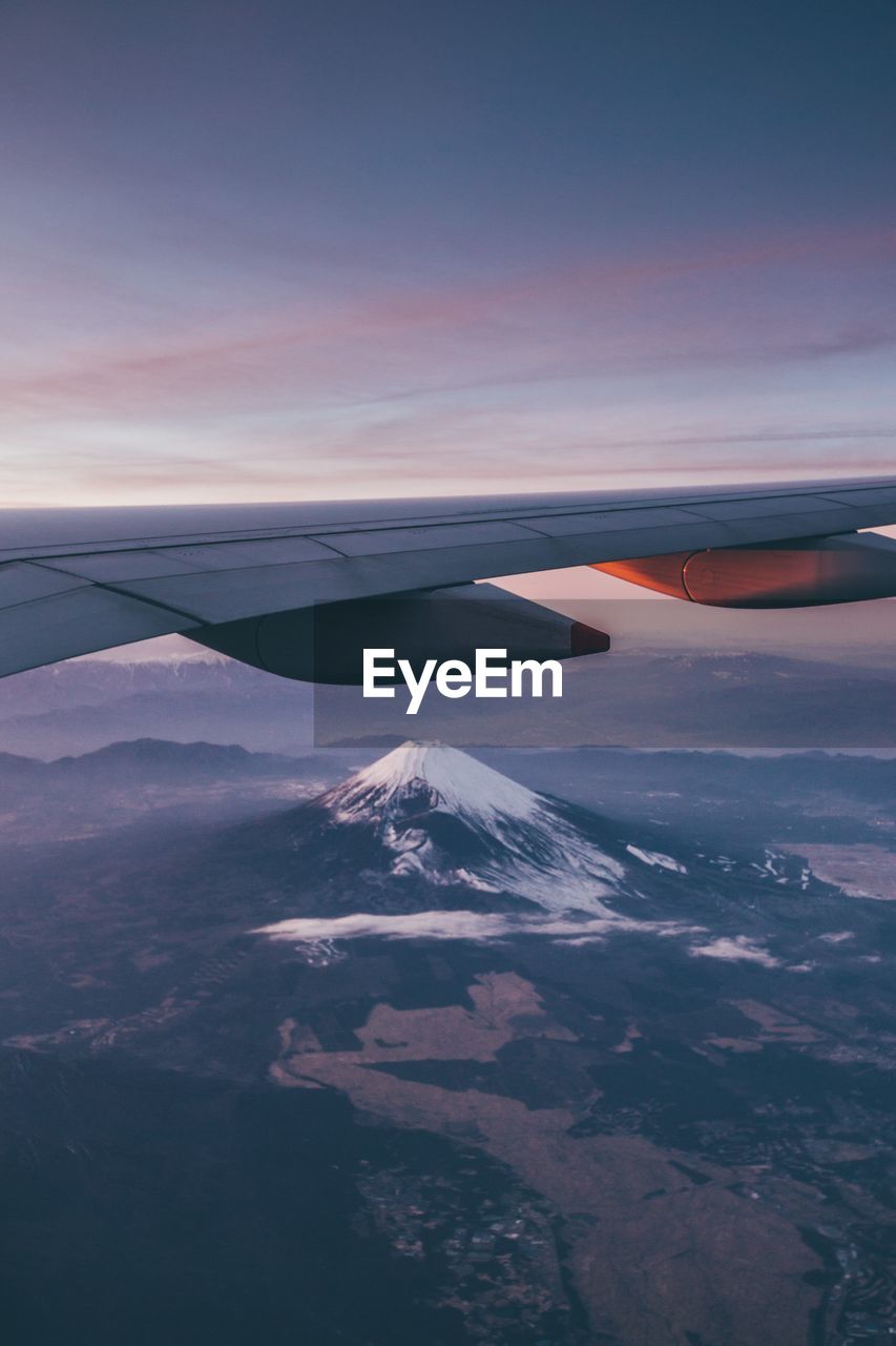 Cropped image of airplane flying over landscape against sky during sunset