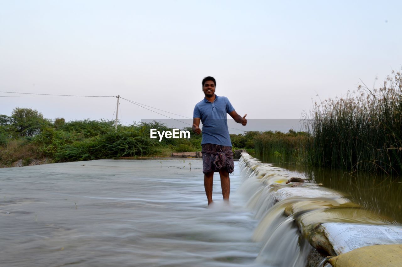 FULL LENGTH OF MAN STANDING IN WATER AGAINST SKY