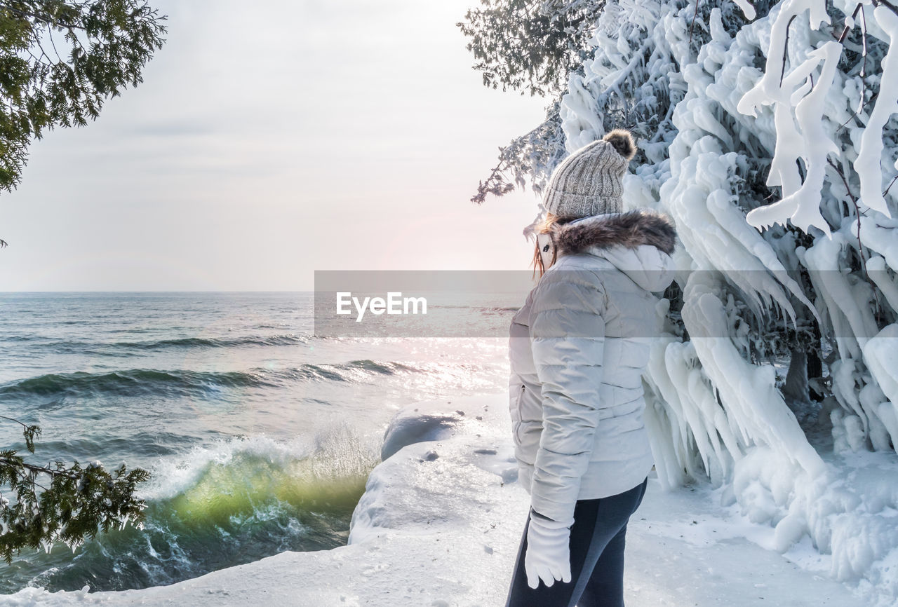 Woman standing by lake against sky during winter