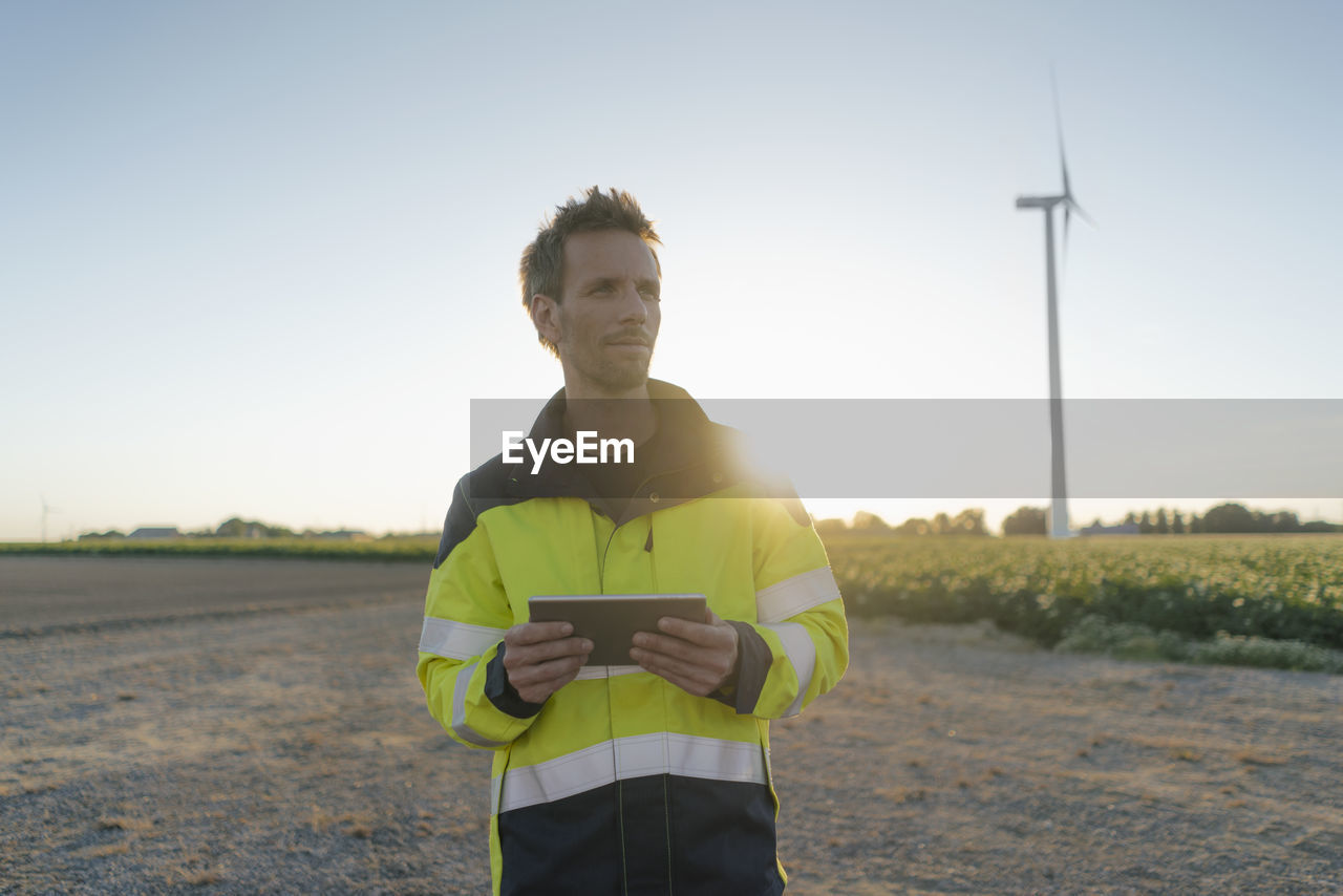 Engineer standing in rural landscape at a wind turbine holding tablet