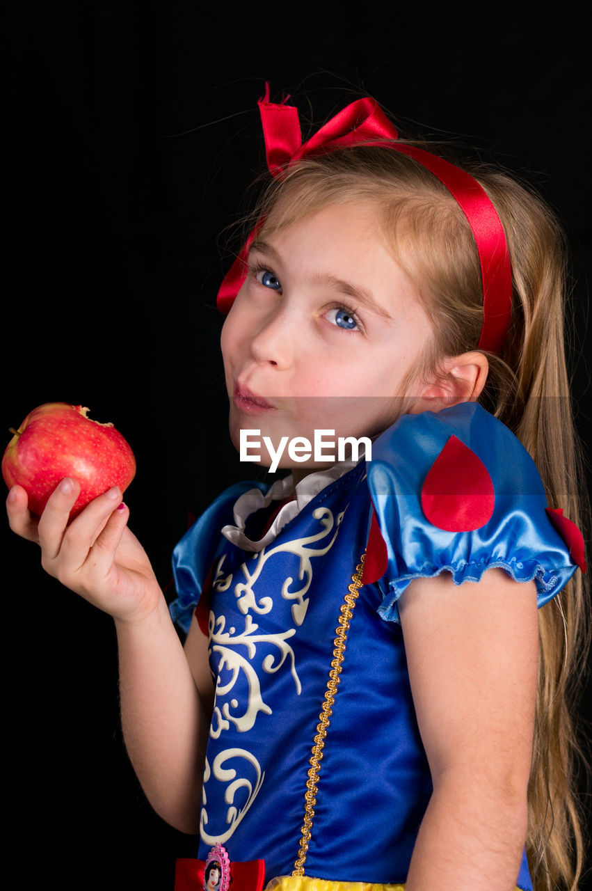 Close-up of girl holding apple against black background