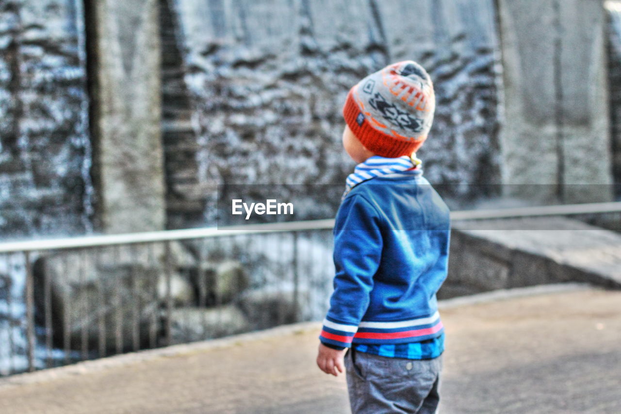 Boy wearing warm clothing standing against waterfall