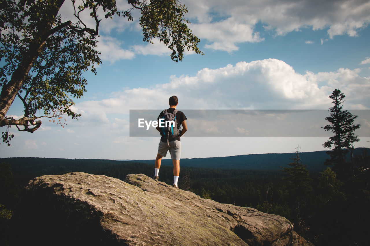 Man standing on top of a rock looking down into a valley in zdarske vrchy in the czech republic