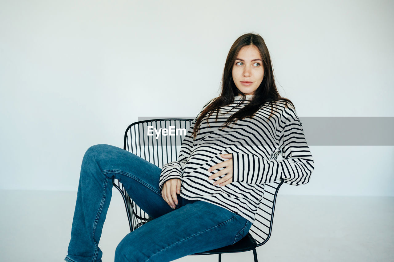 Pregnant attractive woman sits on a chair in the studio.