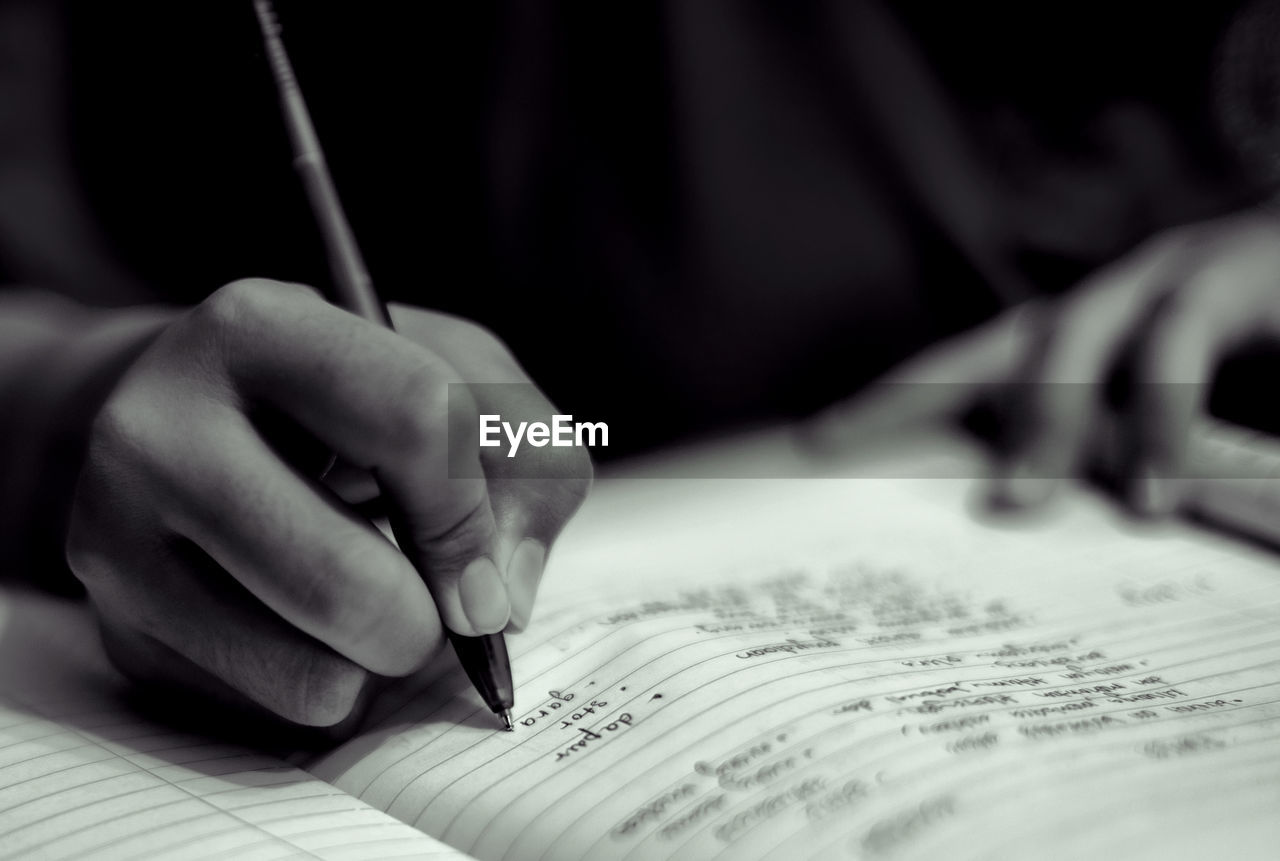 Cropped hand on person writing in book at darkroom