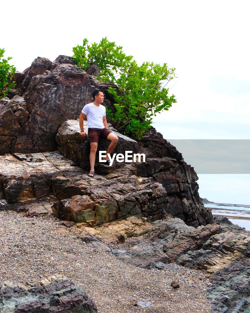 Man standing on rock by sea against sky