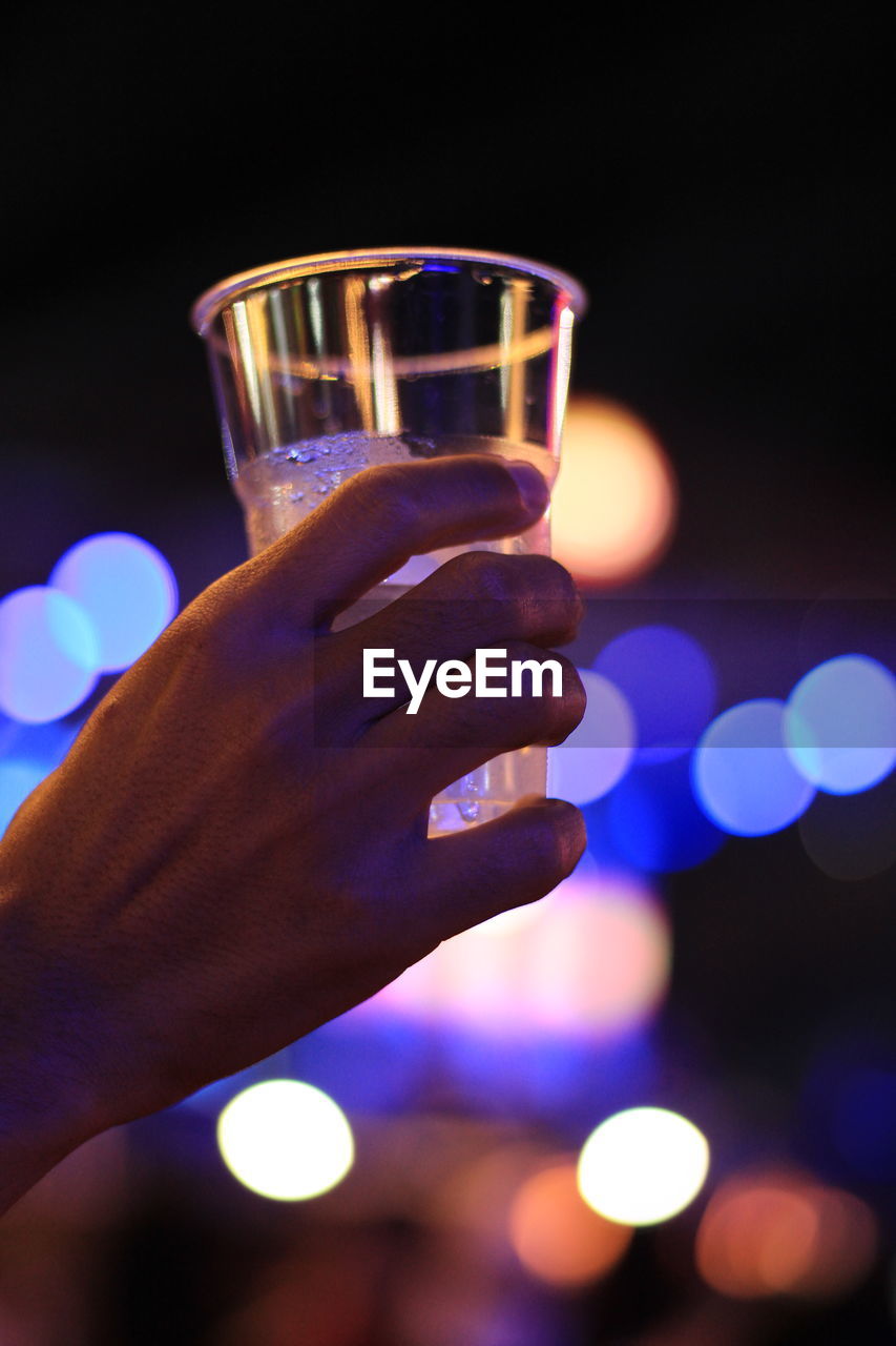 CLOSE-UP OF HAND HOLDING DRINK AGAINST BLURRED LIGHTS