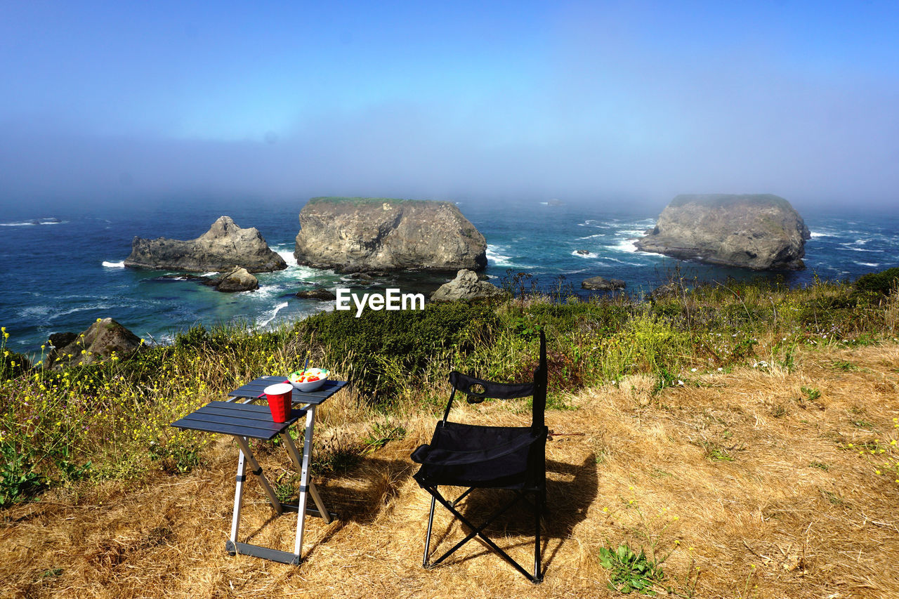 CHAIR ON ROCKS BY SEA AGAINST SKY