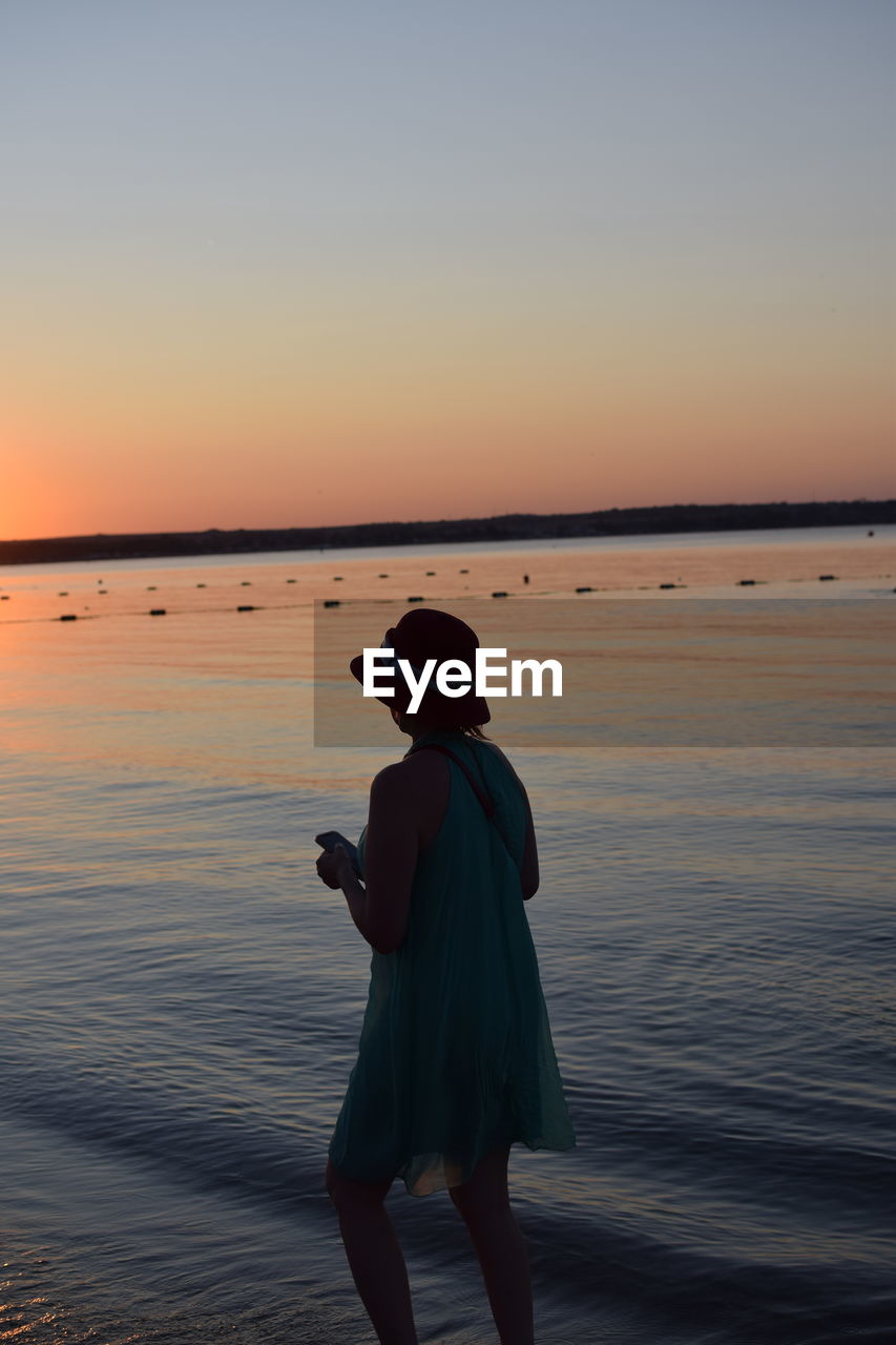 REAR VIEW OF WOMAN STANDING ON BEACH