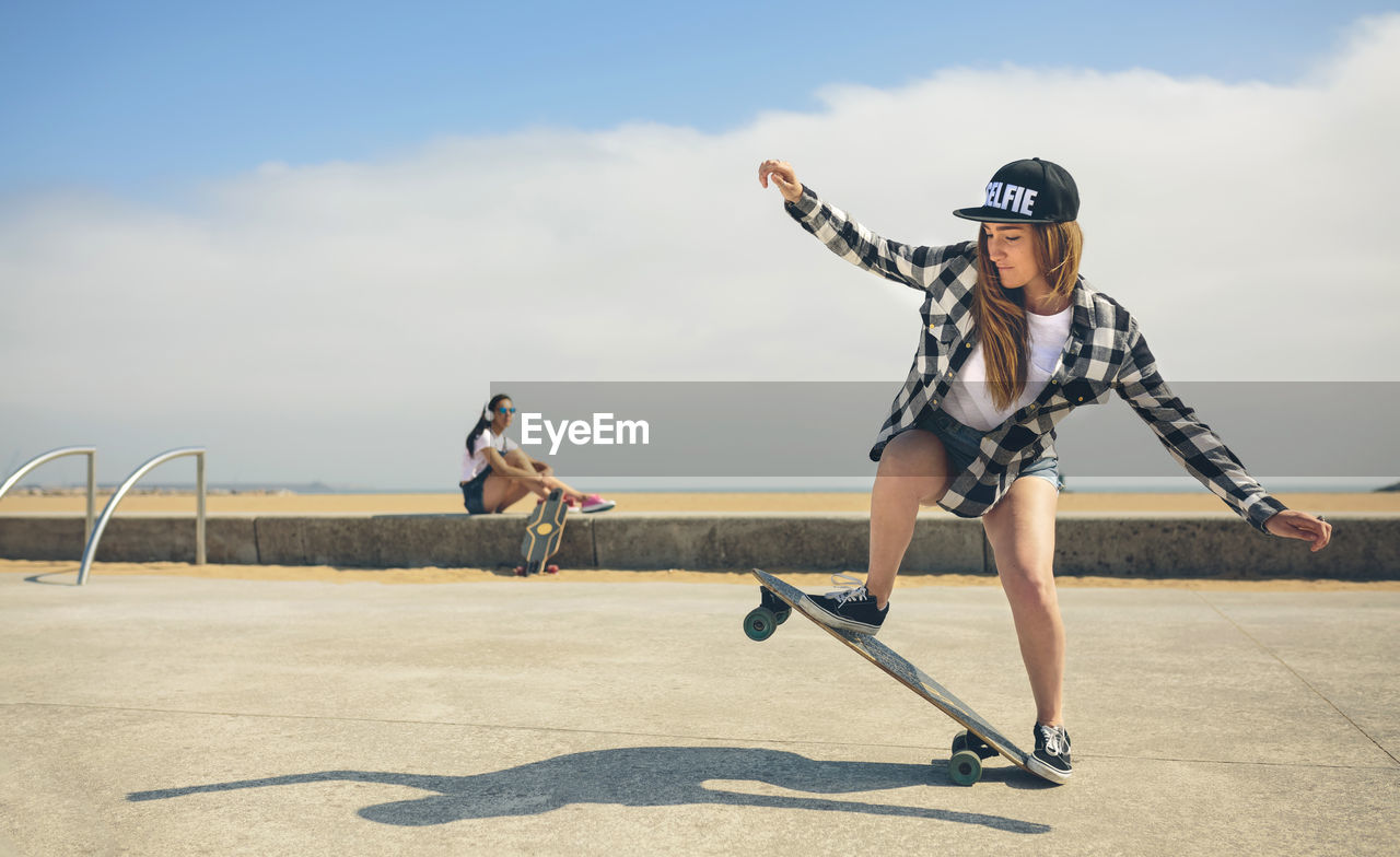 Young woman longboarding while her friend watching her