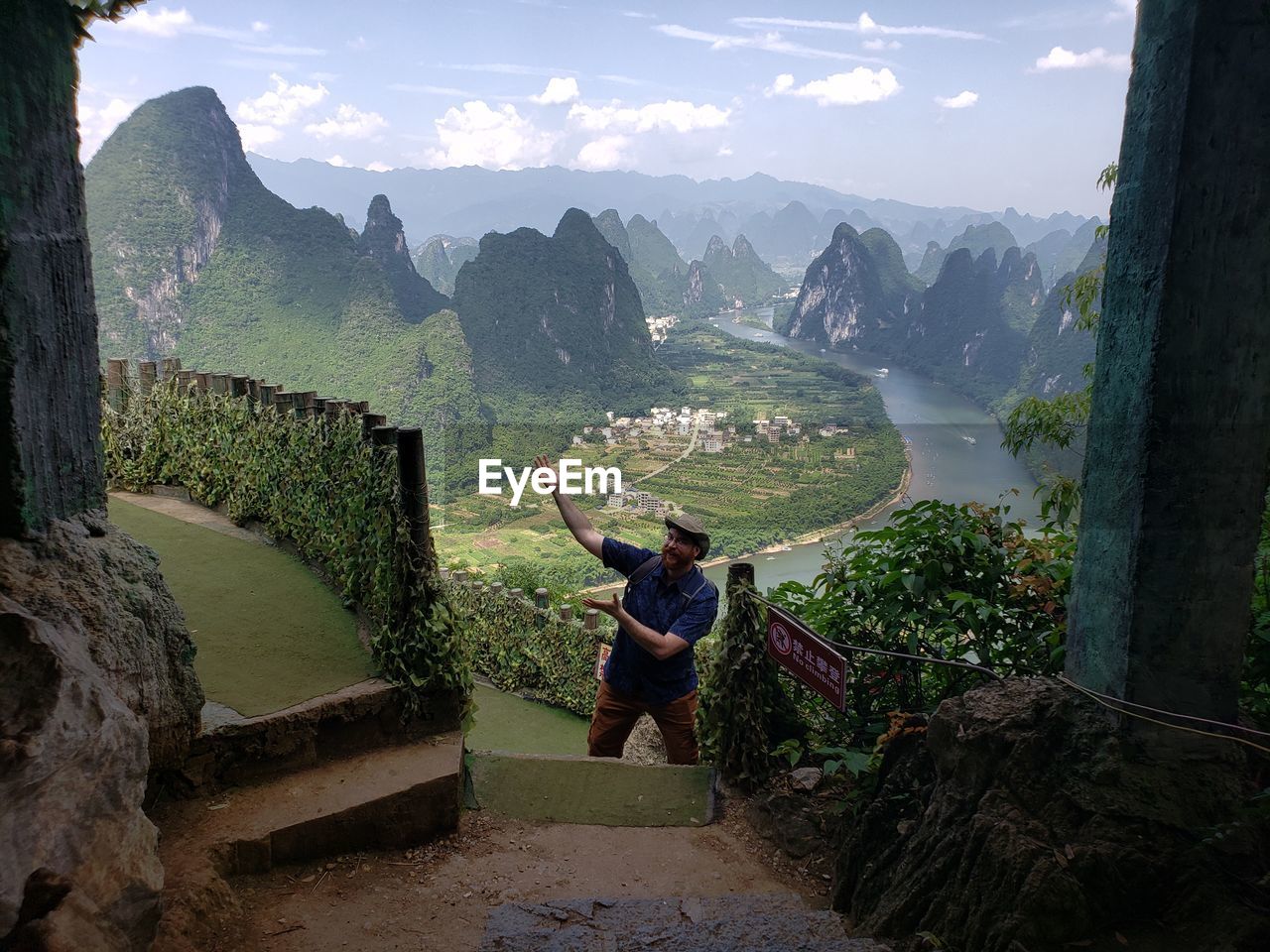 REAR VIEW OF MAN STANDING ON LANDSCAPE AGAINST MOUNTAINS