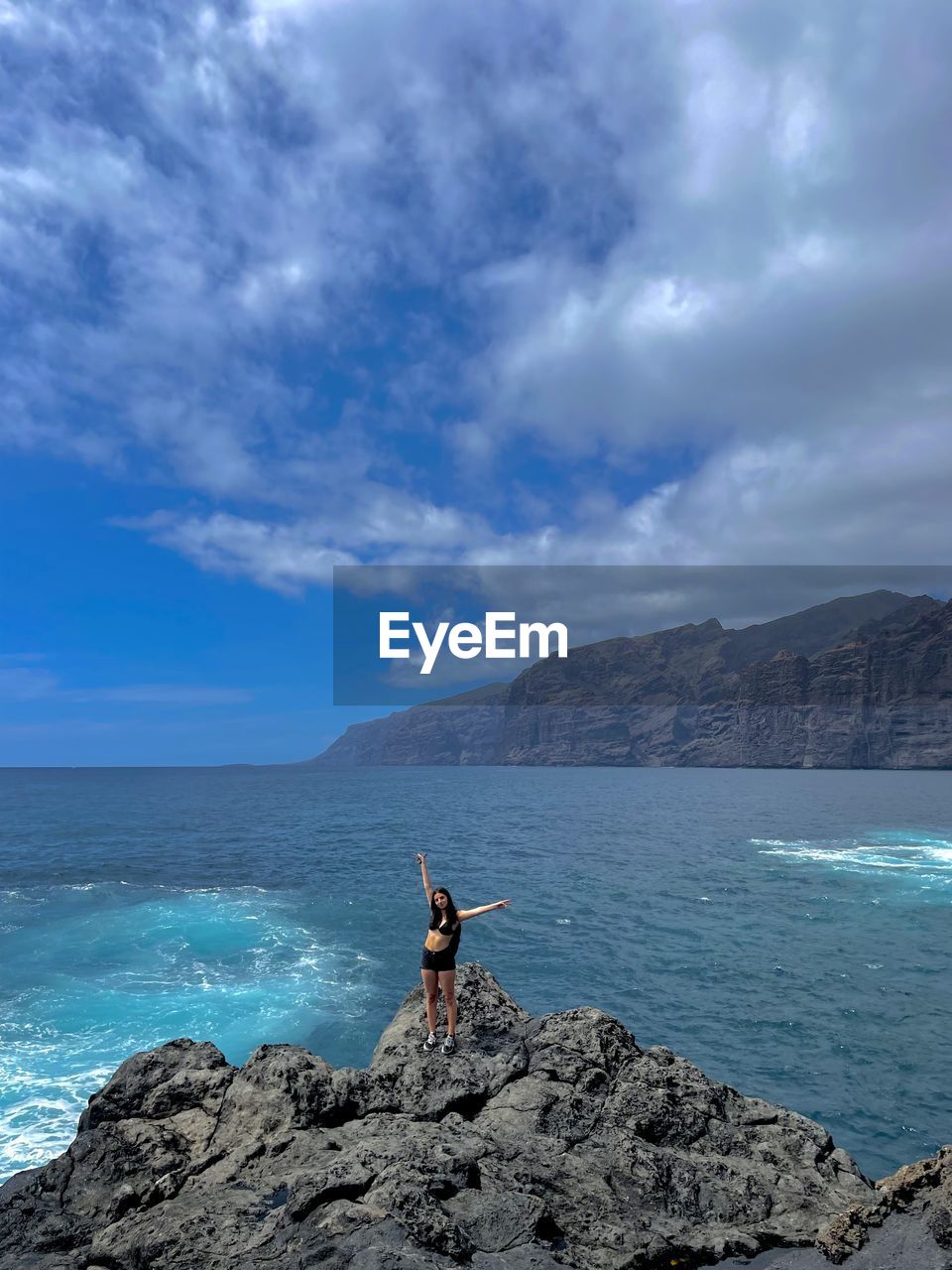 Rear view of man standing on rock by sea against sky