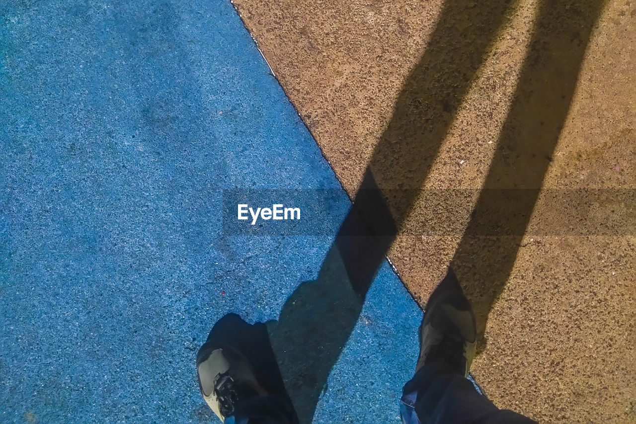 Low section of man standing on road during sunny day