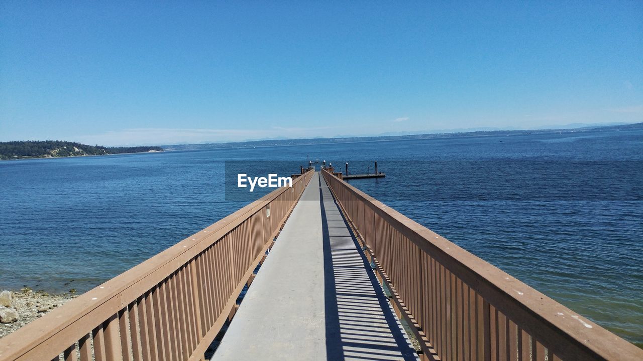 Pier over sea against clear blue sky