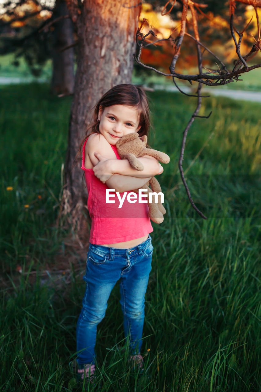 Girl holding stuffed toy and standing on field