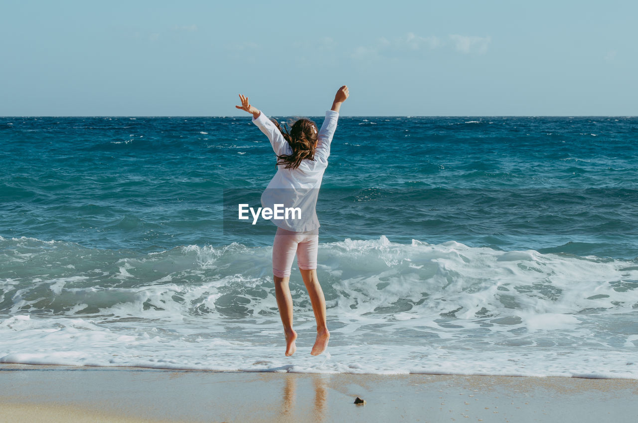 Girl jumping  on beach against sky