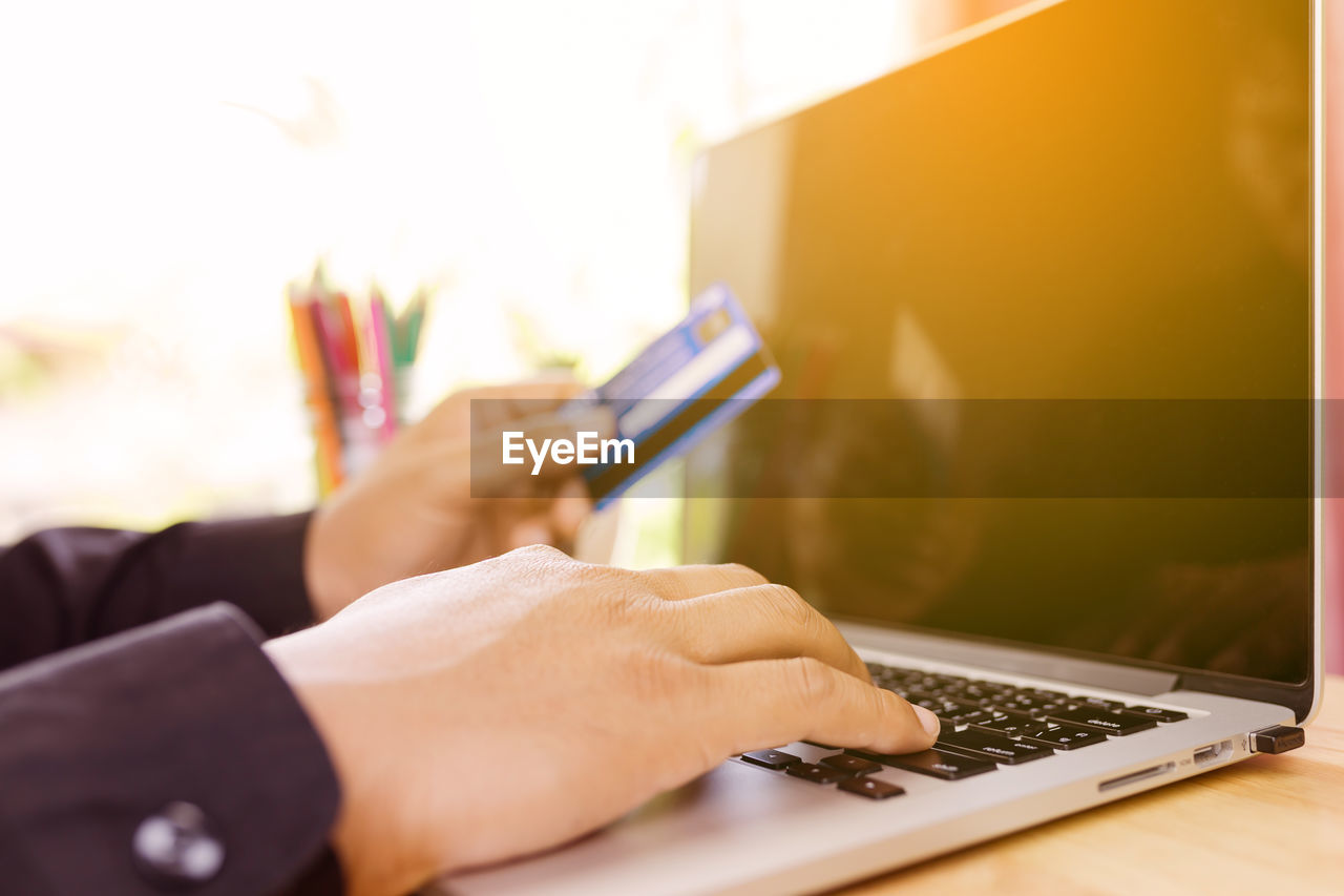 Cropped hands of man holding credit card while using laptop for online shopping on table