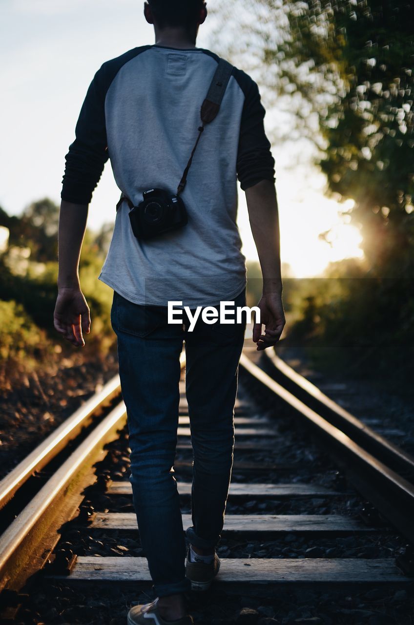 REAR VIEW OF A MAN STANDING ON RAILROAD TRACK