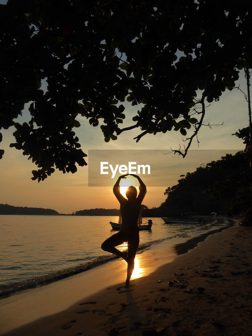 Silhouette woman doing yoga at beach against sky during sunset