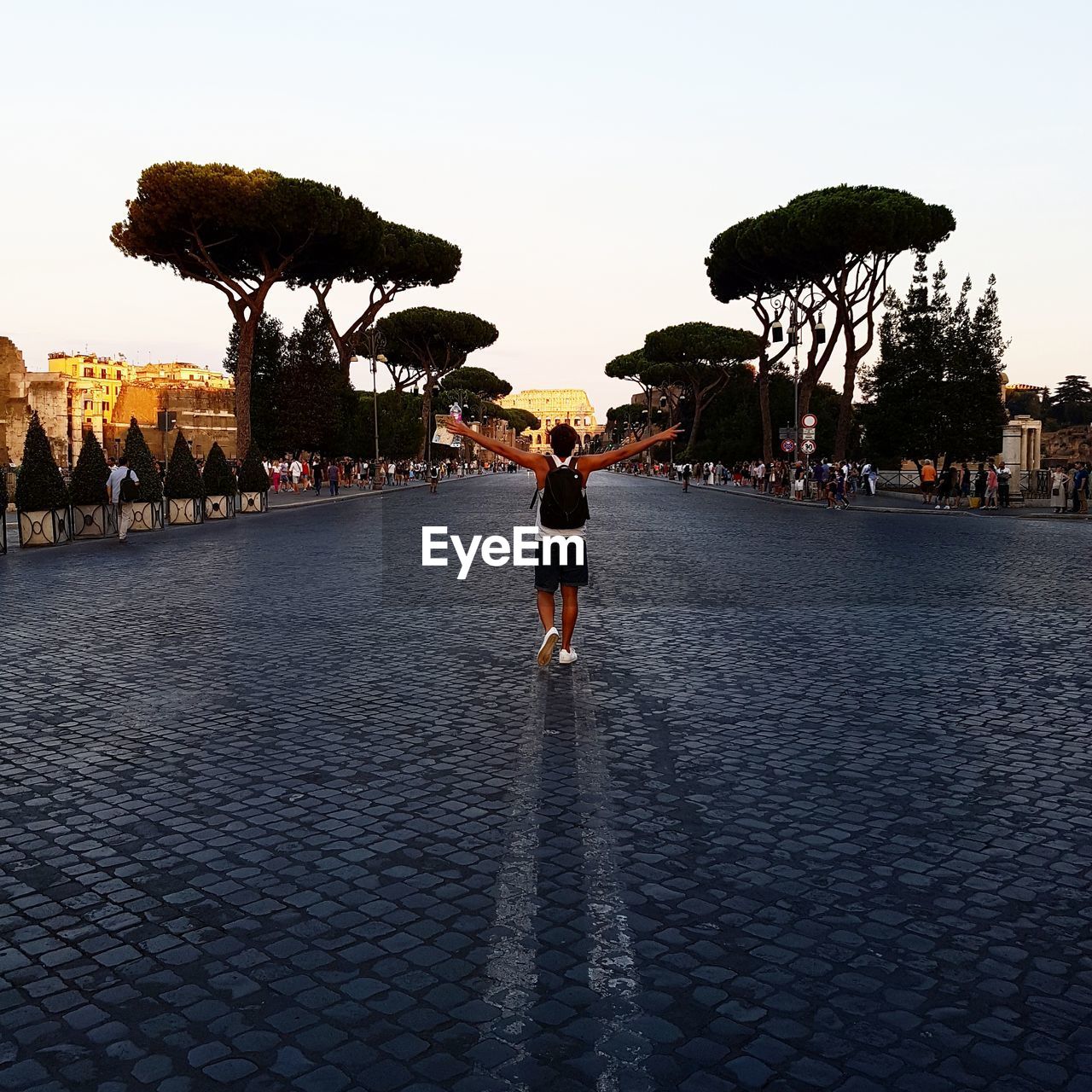 Rear view of man with arms outstretched walking on road