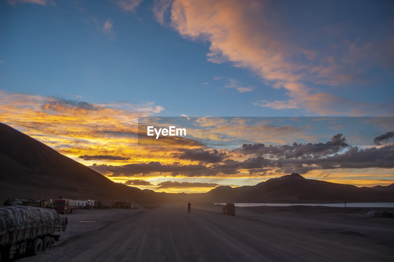 sky, cloud, horizon, sunrise, environment, dawn, transportation, scenics - nature, landscape, nature, beauty in nature, mountain, road, travel, land, sunlight, morning, mode of transportation, travel destinations, dramatic sky, motor vehicle, no people, tranquility, car, sun, mountain range, tranquil scene, outdoors, orange color, tourism, natural environment, non-urban scene, the way forward, blue, afterglow, desert, journey, cloudscape