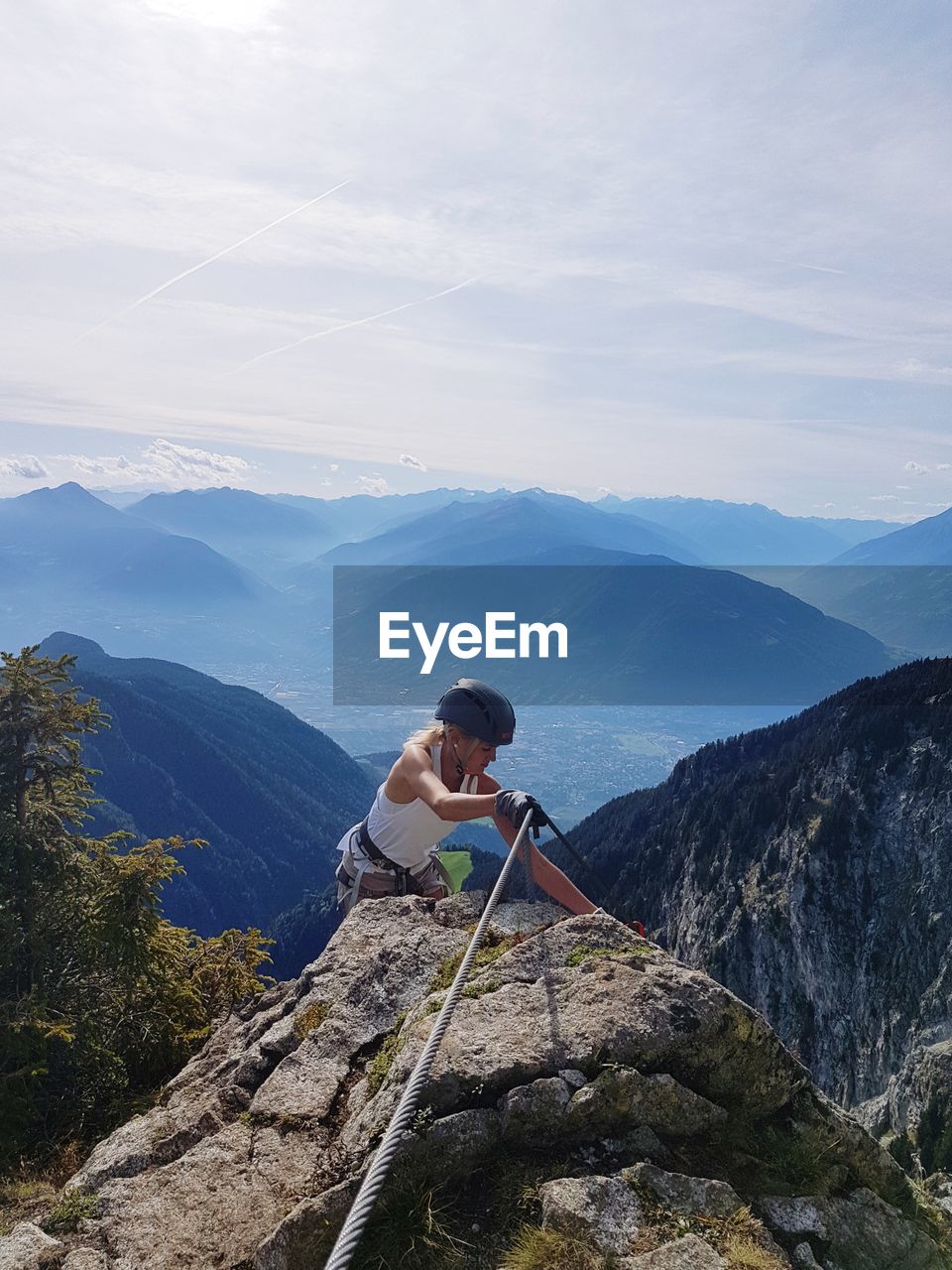 Woman climbing on rock by mountains against sky