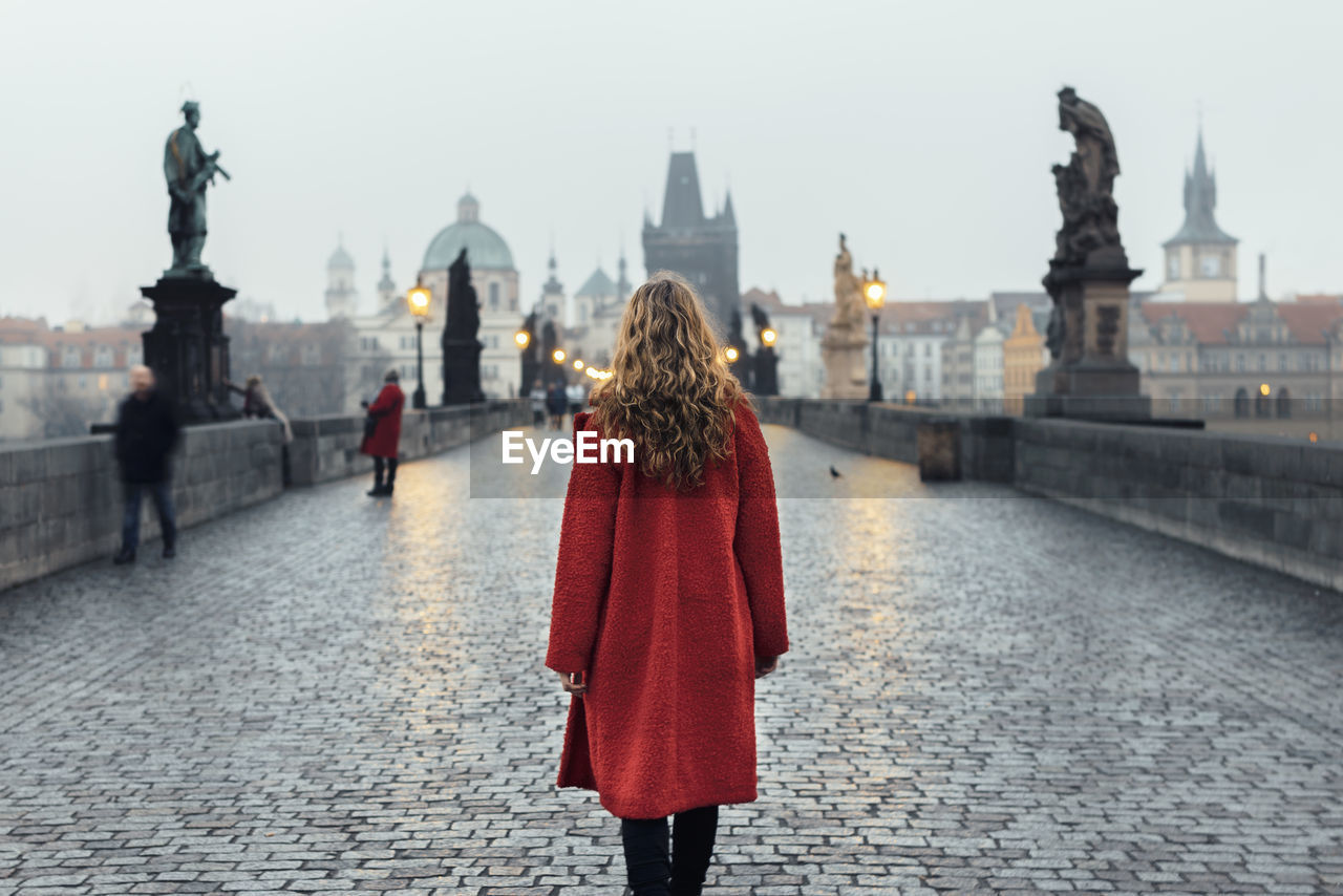 Rear view of woman walking on bridge by street lights at sunrise