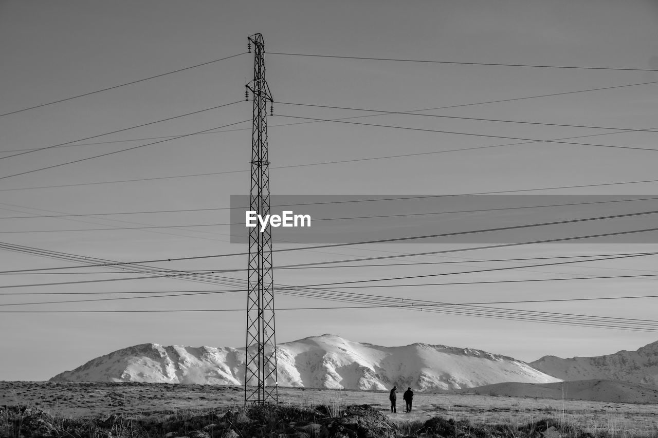 Electricity pylons on snowcapped mountain against sky