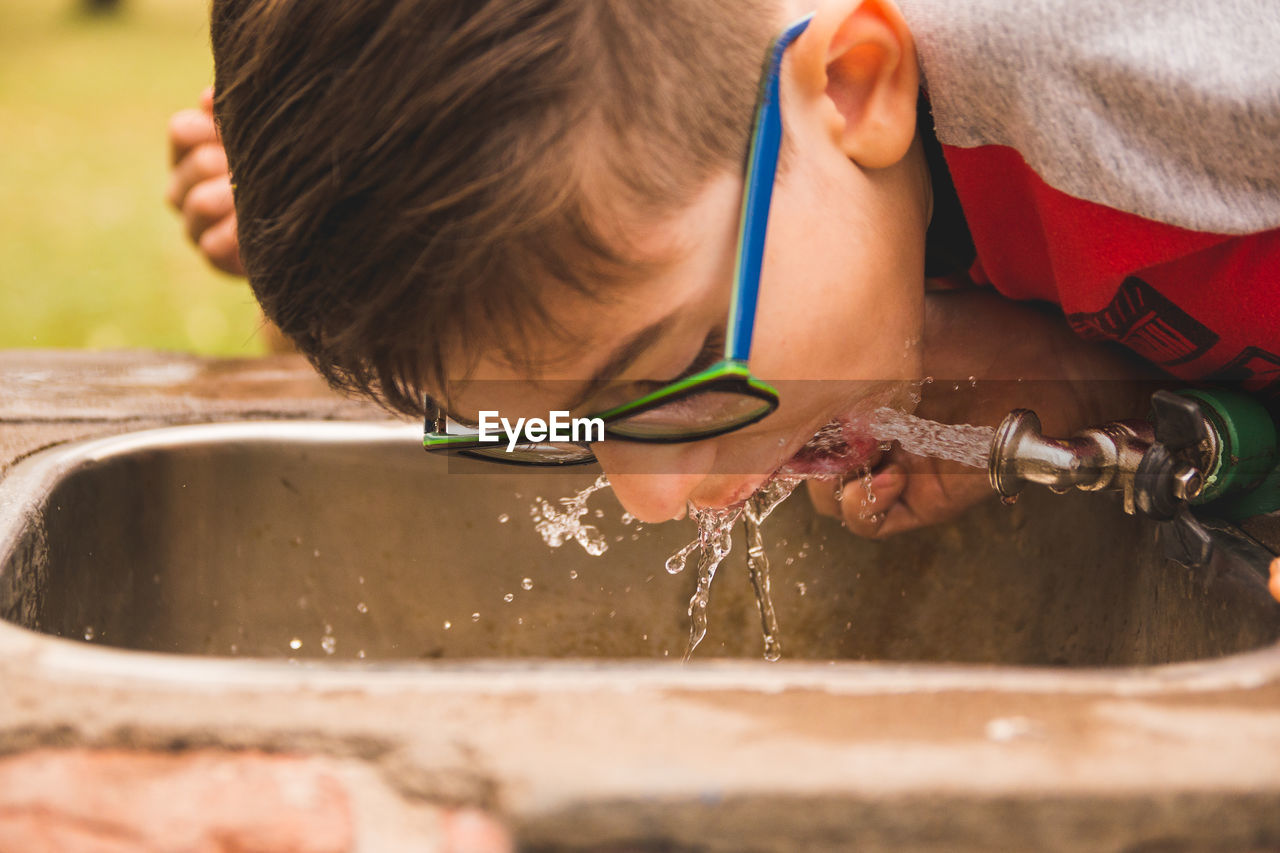 Close-up of boy drinking water from faucet