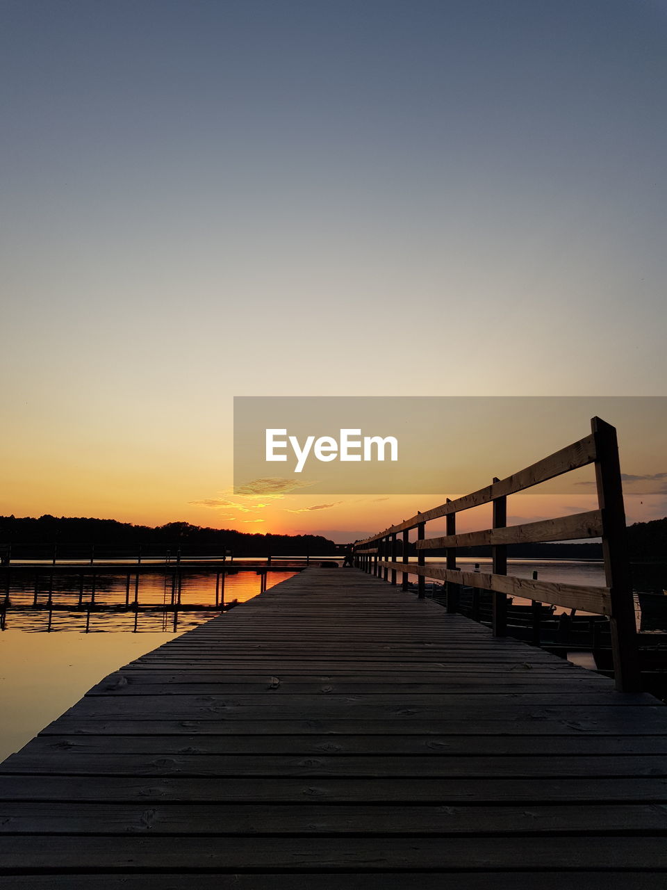 PIER AMIDST LAKE AGAINST CLEAR SKY DURING SUNSET