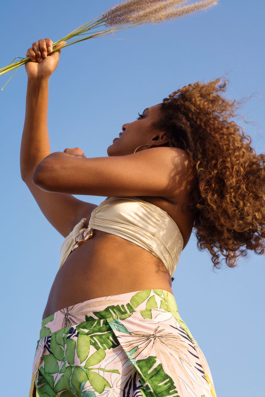 Low angle portrait of young woman with dark skin and long curly hair at the beach