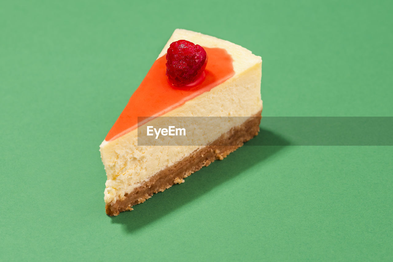 Cheesecake slice with raspberry syrup and cracker crust isolated on a green background, close-up.