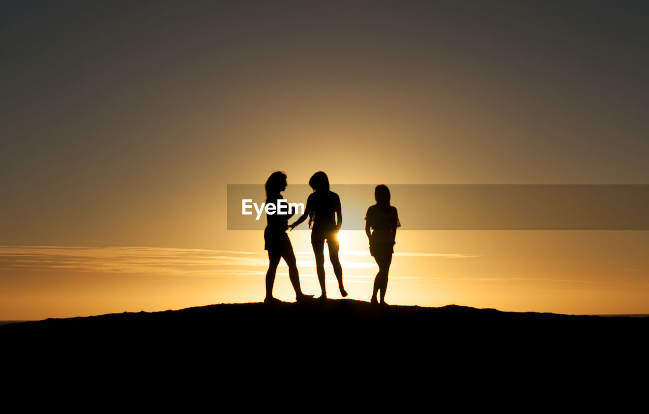 Silhouette women standing on hill against sky during sunset