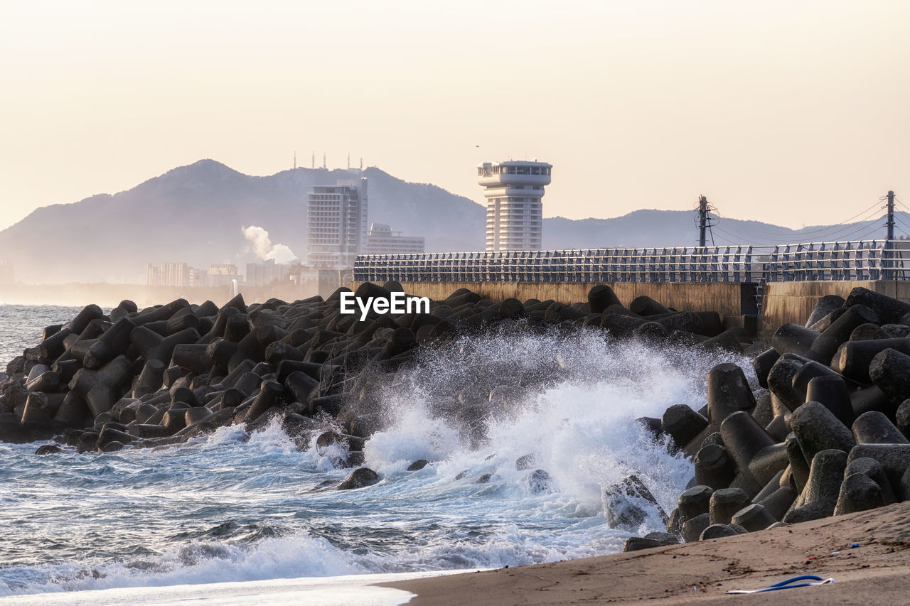 shore, water, wave, sea, coast, breakwater, ocean, land, beach, motion, sky, architecture, nature, rock, body of water, built structure, sand, environment, wind wave, beauty in nature, outdoors, building exterior, no people, power in nature, tower, scenics - nature, morning, bay, travel destinations, sports