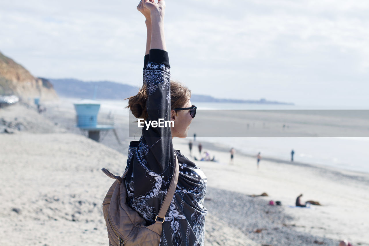 Woman with arms raised at beach against sky