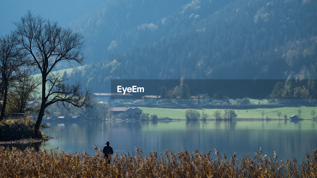 REAR VIEW OF PERSON STANDING ON LAKE AGAINST SKY
