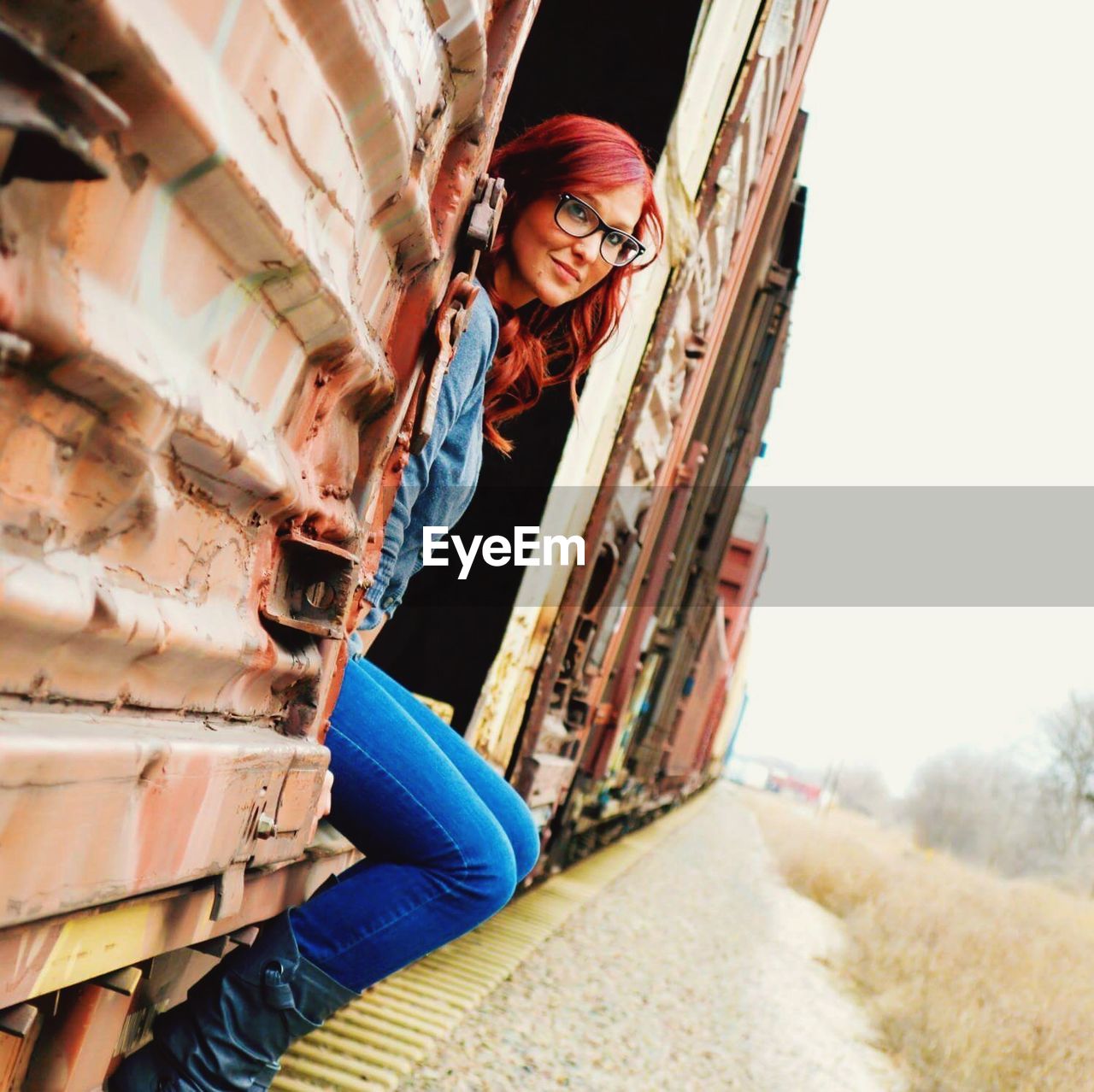 Smiling young woman sitting in freight train against clear sky