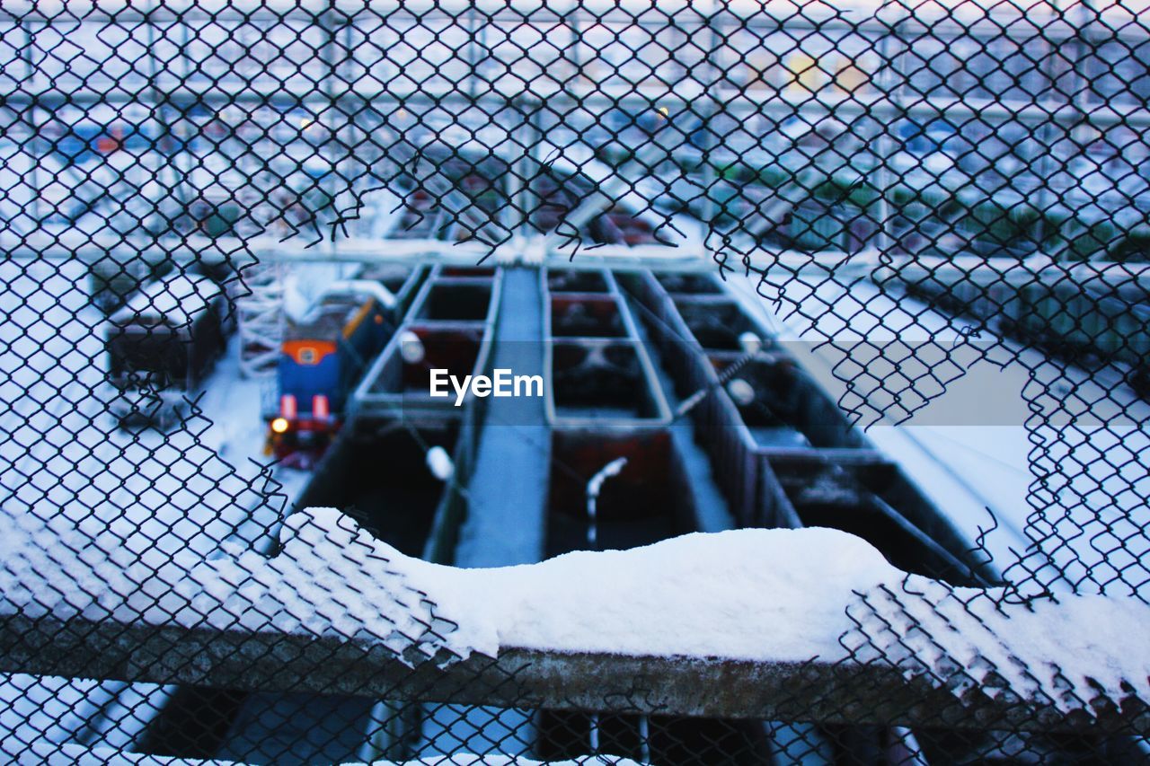 High angle view of trains on snow covered field seen through broken fence