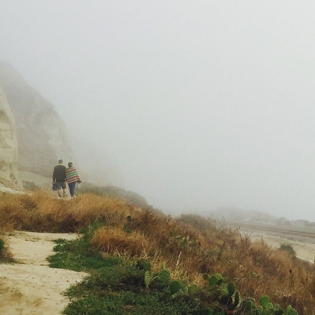 Rear view of couple walking at beach in foggy weather