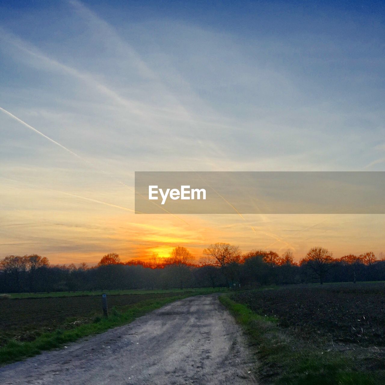 ROAD AMIDST FIELD AGAINST SKY AT SUNSET