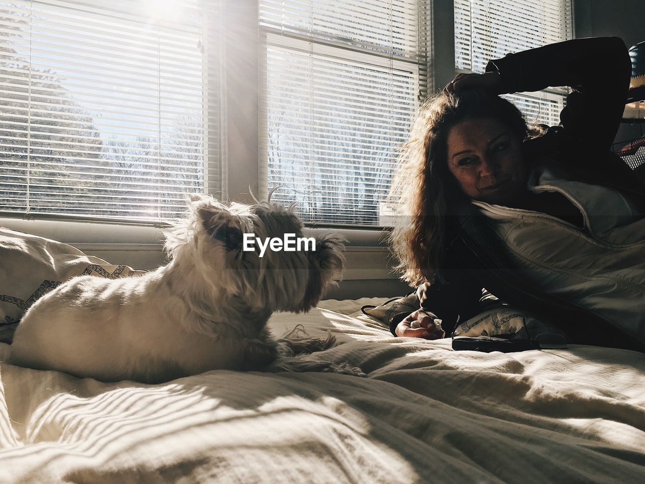 Woman looking at dog relaxing on bed