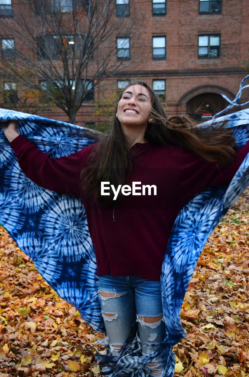 Young woman holding shawl while standing at park during autumn