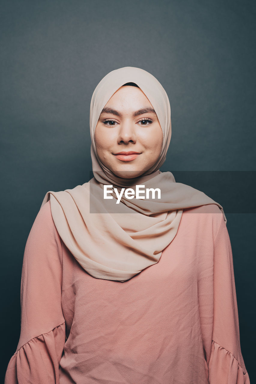 Portrait of smiling young woman wearing hijab against gray background