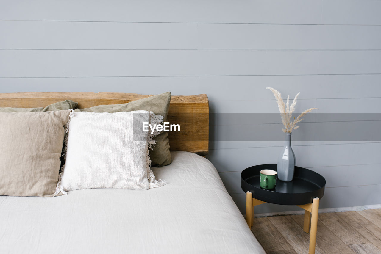 Black modern bedside table next to the double bed with grey bedding in a simple bedroom interior