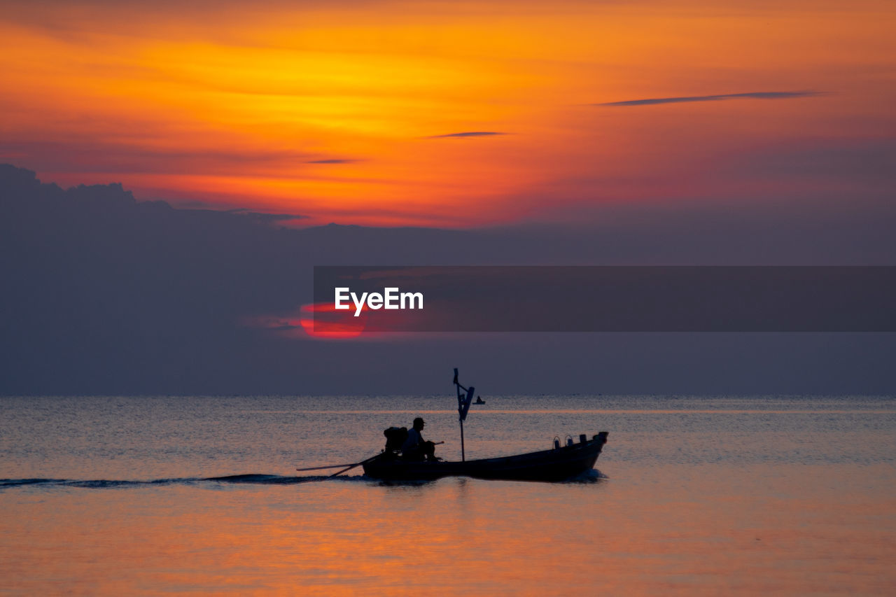 Silhouette man sitting in fishing boat on sea during sunset