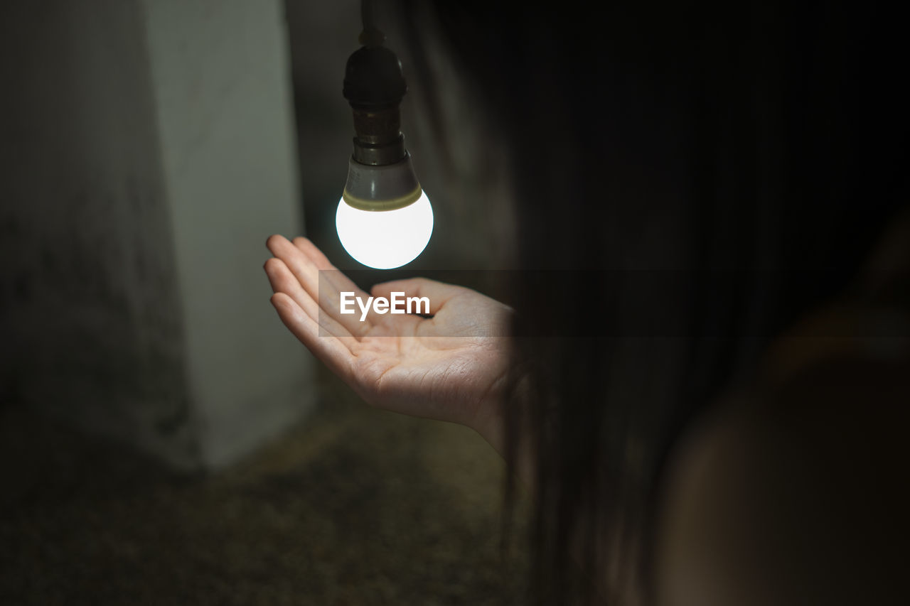 Close-up of woman hand under light bulb at home