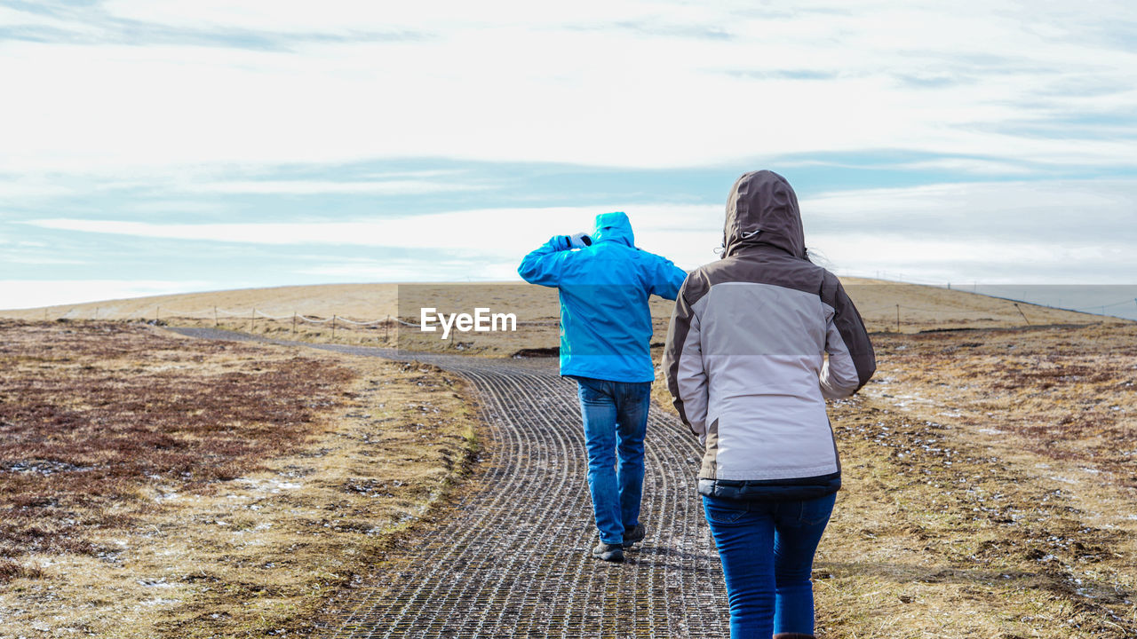 Rear view of man and woman walking on land against sky