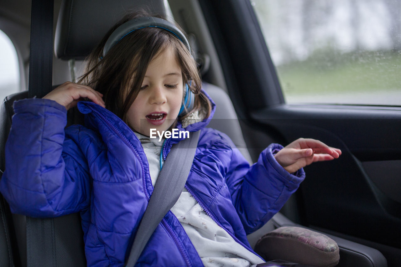 A little girl listens to music on headphones in a car on a car trip