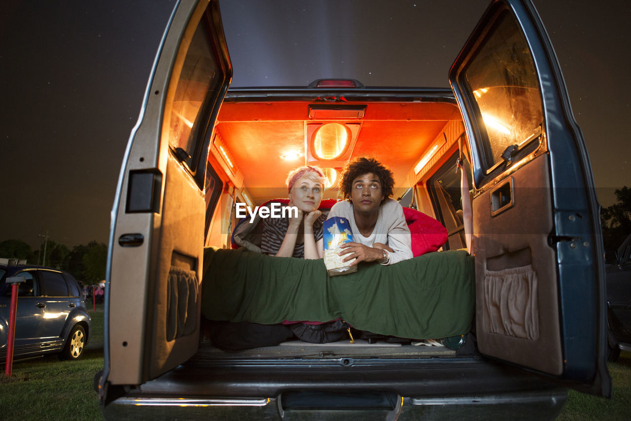 Couple holding popcorn while sitting in camping van during drive-in movie