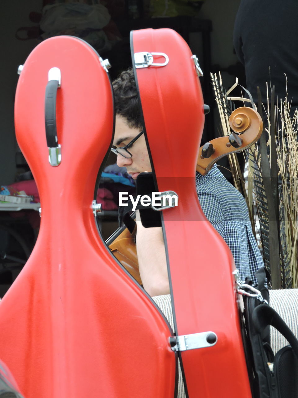 Side view of man playing cello seen through red case